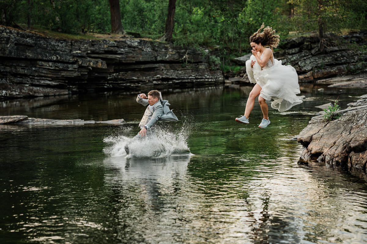 Bride and groom jumping in a green colored river in their wedding attire on the day of their elopement in Alta Norway
