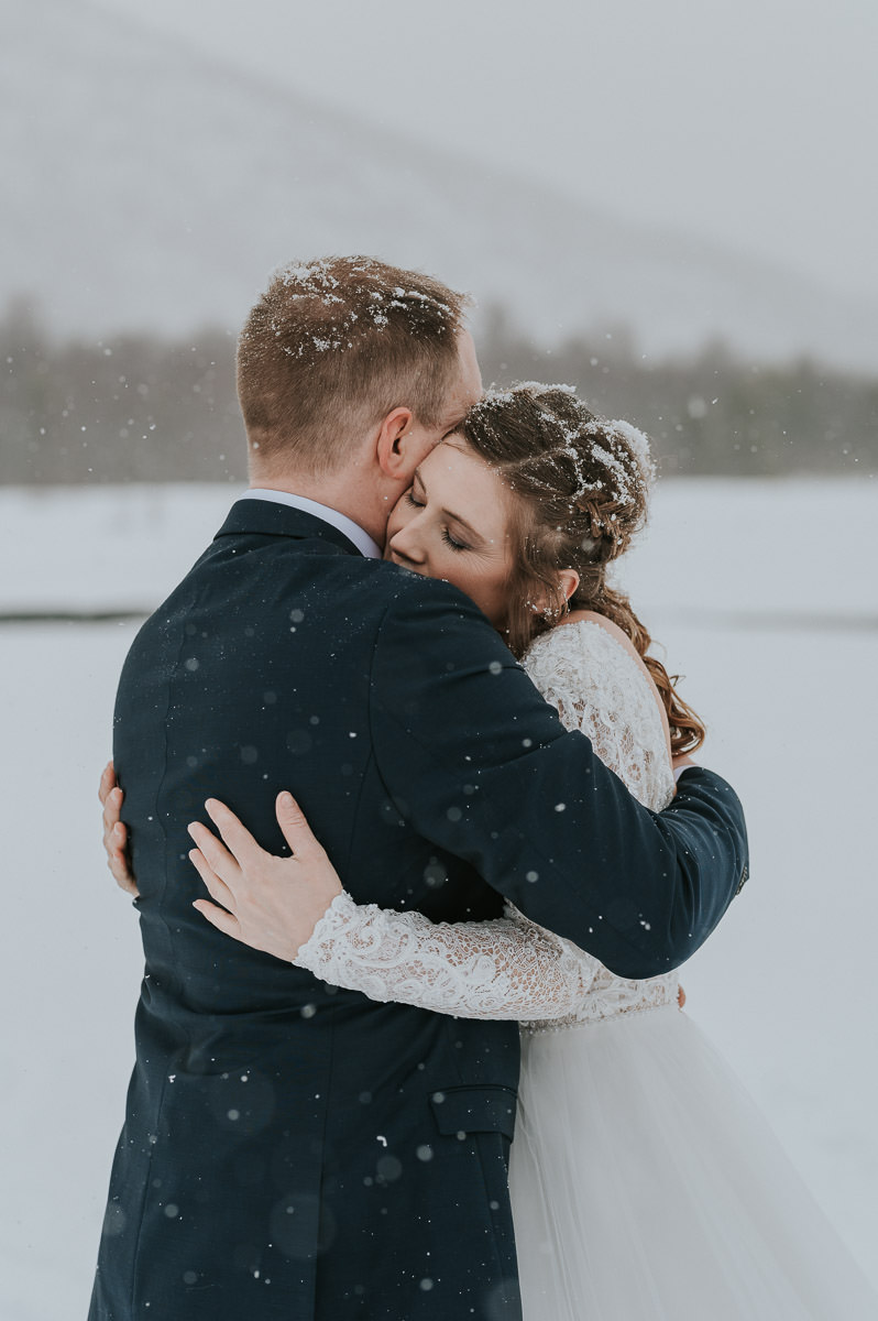 Bride and groom hugging each other among beautiful winter landscape under a snowfall in Alta Norway