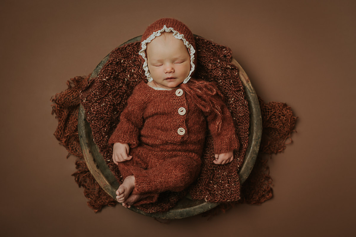 Nydelig nyfødt jente sover i en kurv på brun fotobakgrunn