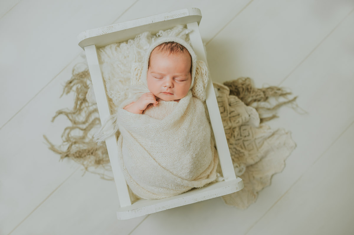 Nyfødt jente i hvite farger sover i en dukkeseng på nyfødtfoto i Alta hos TS Foto Design
