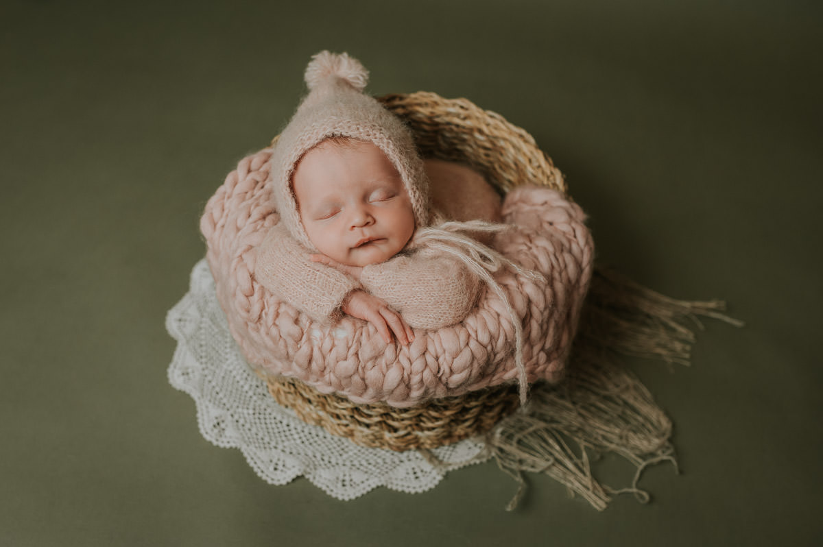 Nyfødt jente i rosa ulldrakt sover søtt i en kurv på grønn bakgrunn