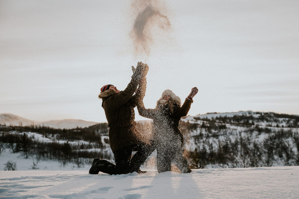 Cute couple playing with a sniw on the day of their Winter engagement photoshoot in mountains of Alta Norway - wedding photographer TS Foto Design 