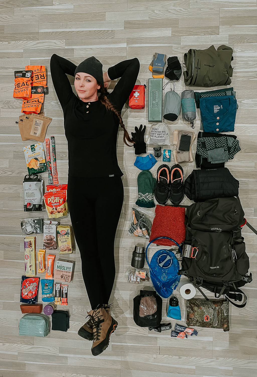 Young woman laying on a floor among different hiking gear prepped for adventures in Norway