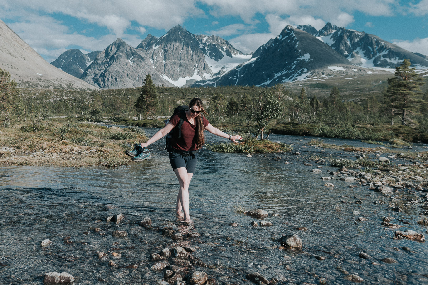 Adventure photographer Tanja Skoglund walks through the river barefoot with a stunning view of Lyngen Alps in Troms Norway