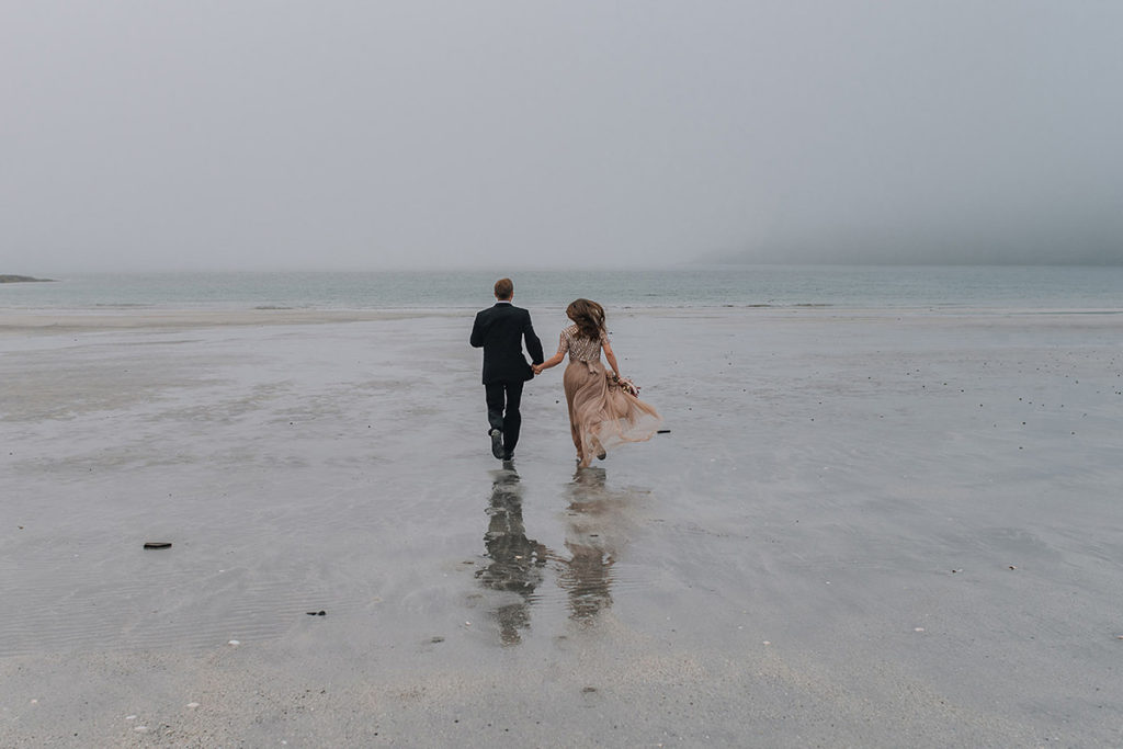 Adventurous bride and groom running on a white beach on a foggy night in Sørøya Norway by elopement photographer TS Foto Design