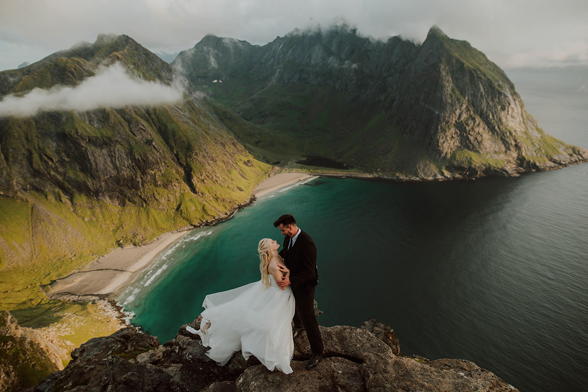 Portrait of a bride and groom standing on a mountaintop in the sunset among spectacular scenery of Lofoten in Norway