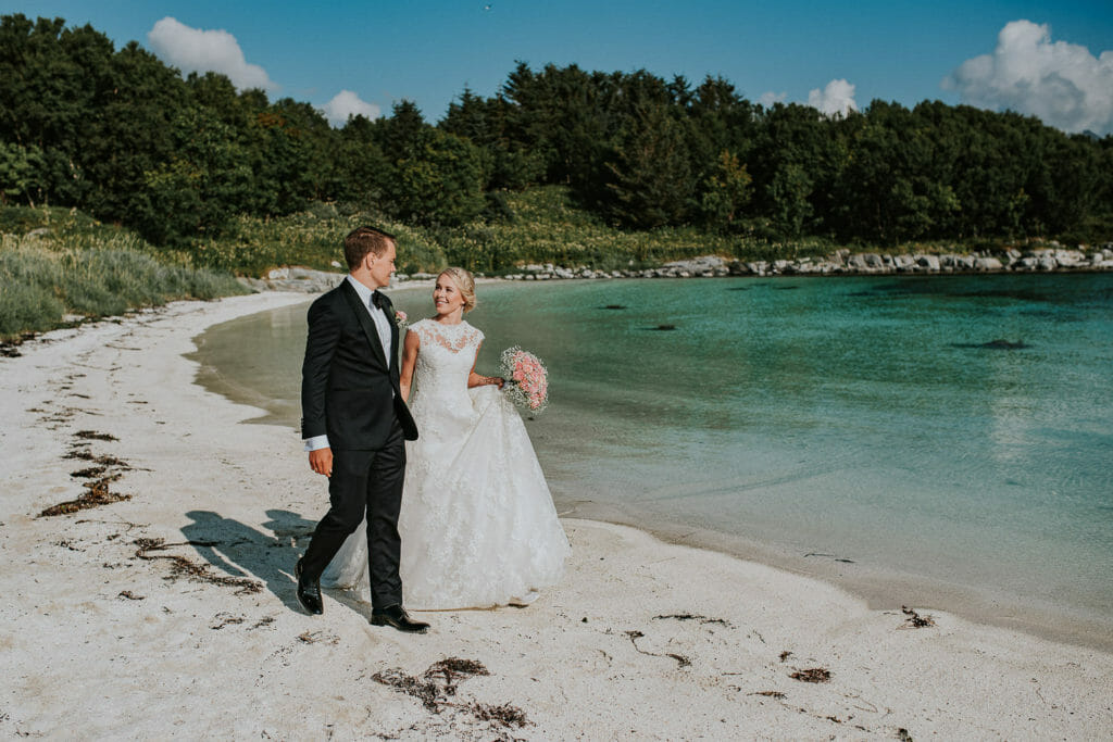 Bride and groom walking on a beautiful secluded  beach in Senja Norway with white sand and crystal clear water