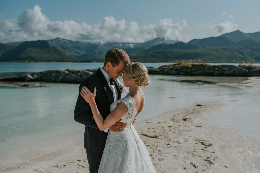 Young and beautiful bride and groom enjoy an intimate moment at the white sand beach of secluded island on Senja, Norway