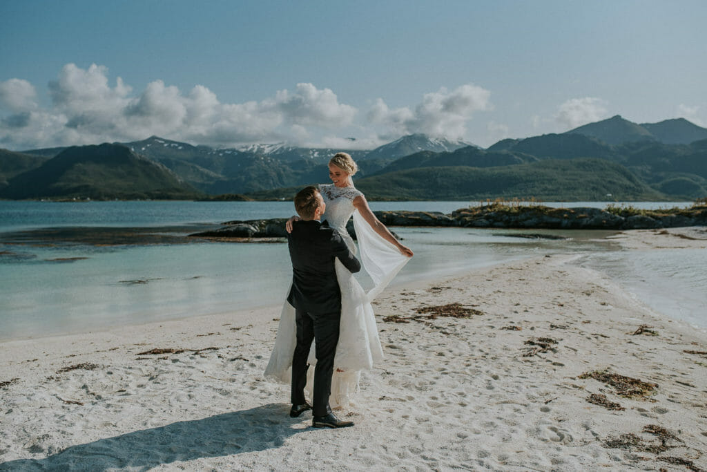 Groom lifts his bride and swirls her around on a beautiful secluded beach in Senja, northern Norway - perfect location for a private intimate wedding ceremony