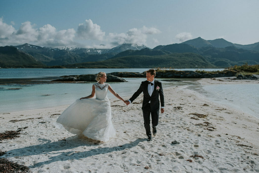 Bride and groom running on a white sand beach on a warm sunny day at Senja, Norway