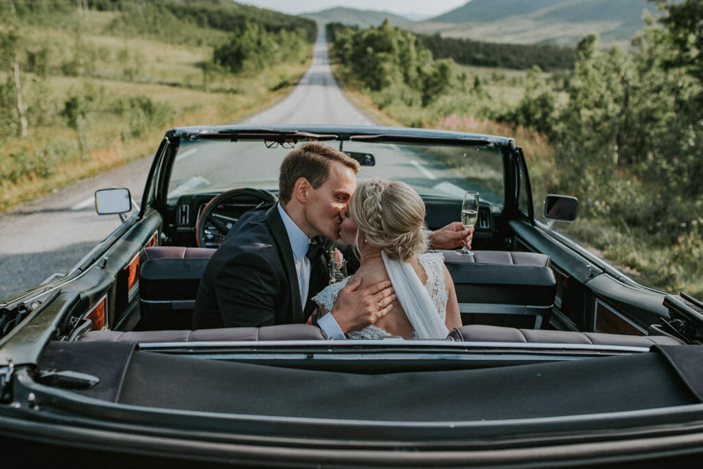 Bride and groom kissing in vintage cbriolet on the way to their wedding party at Varden bygdehus at Senja, Troms