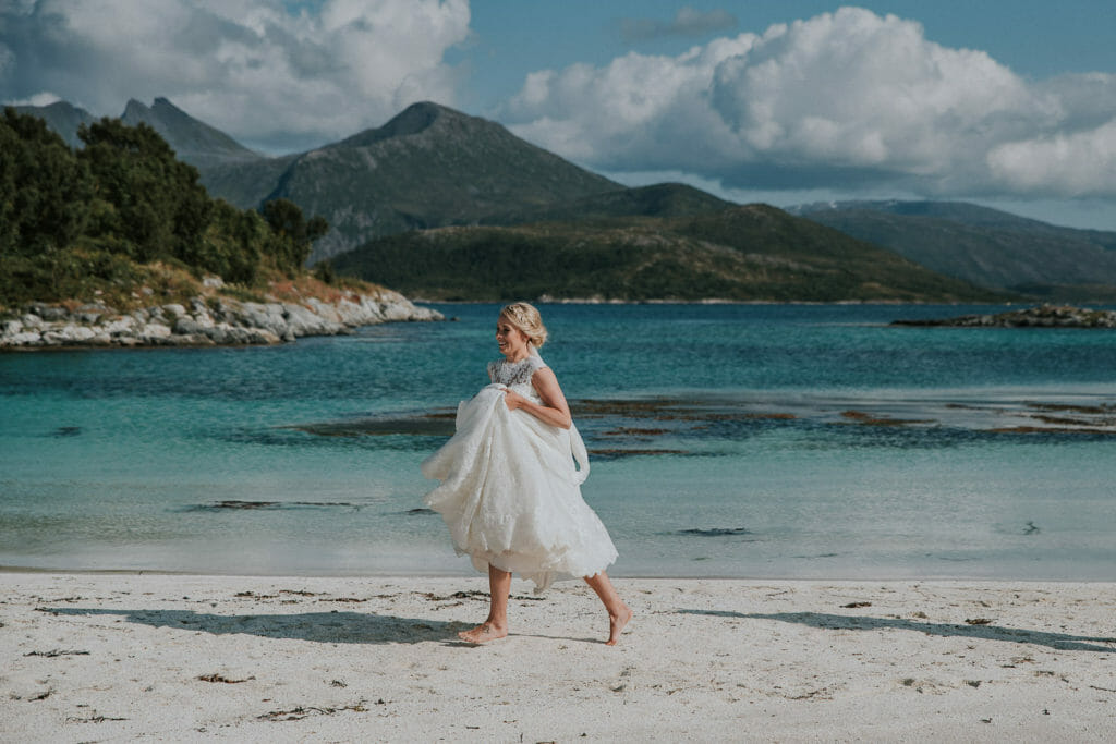 Barefoot and happy bride running at the beach of Senja