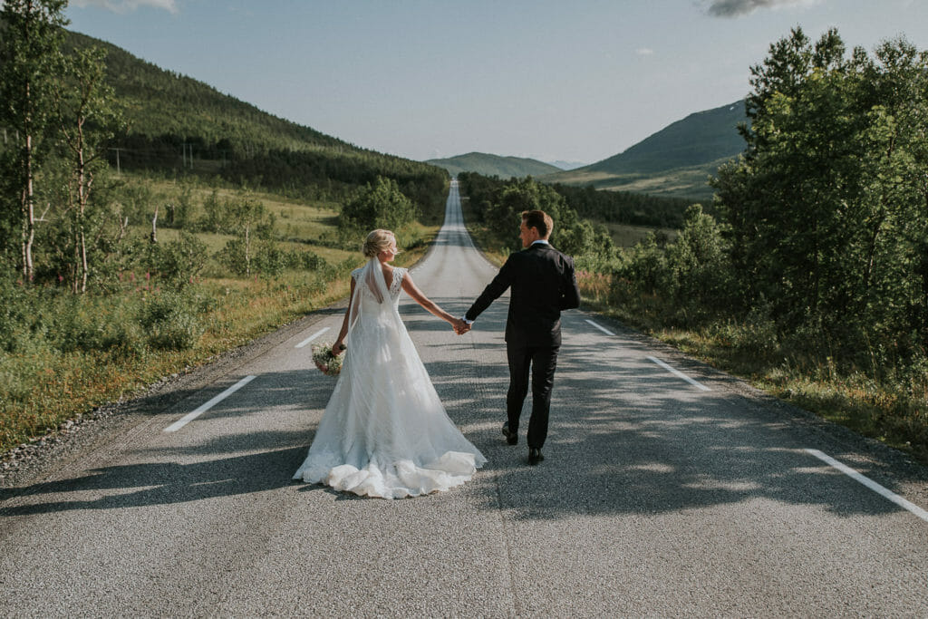 Bride and groom walking on an empty highway towards the horizon 