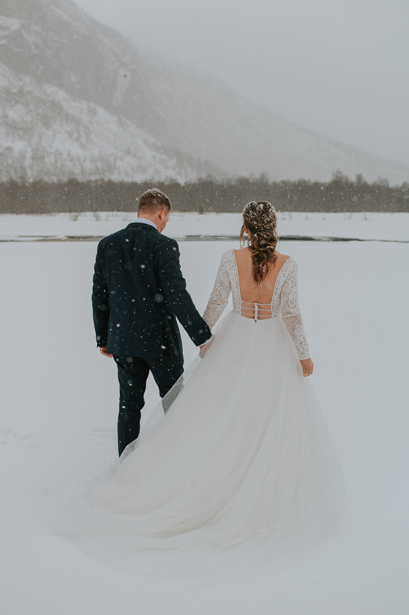Brudepar spaserer blant fantastiks vinterlandskap mens snøen daler
