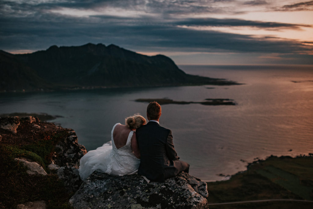 Bride and groom sitting on a mountain top enjoying sunset with amazing view to mountais of Lofoten Norway