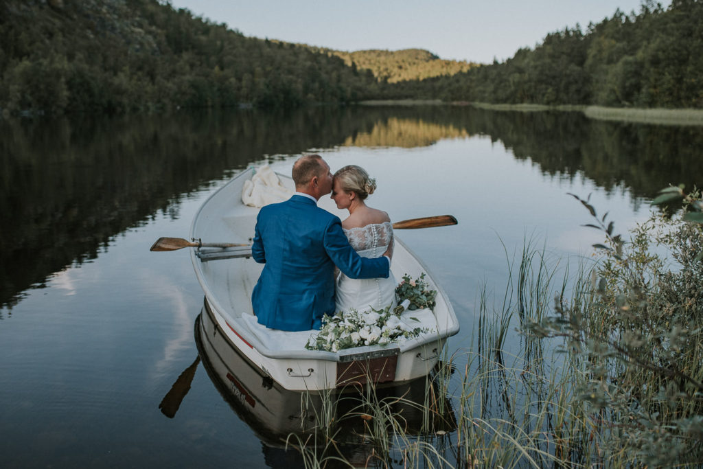 Nydelig øyeblikk der brudgom kysser sin brud mens de ror båt på en rolig innsjø i Alta på en sensommer bryllupsdag