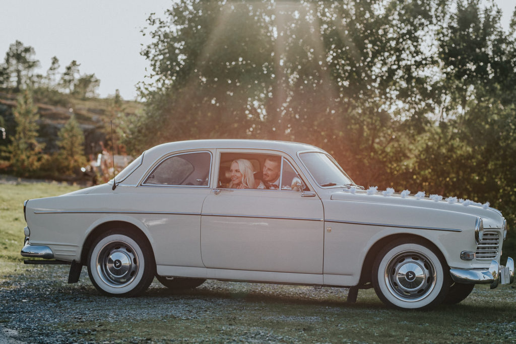 Flott brudepar i vintage bil retrobil vinker farvel i nydelig kveldssol