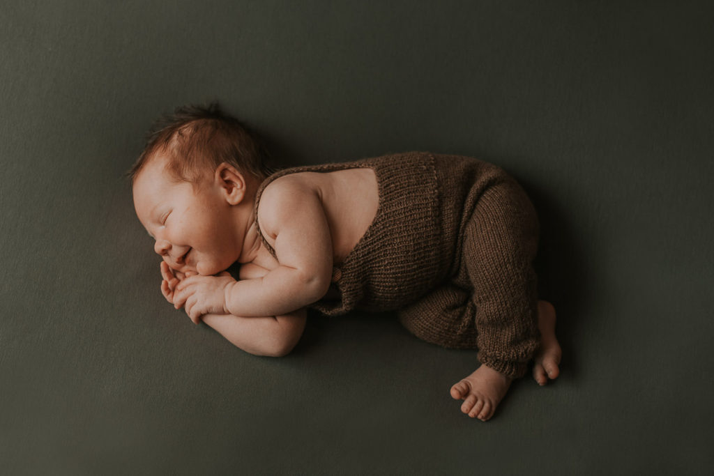 Skjønn nyfødt gutt ligger på mørkegrønn bakgrunn og smiler i søvne