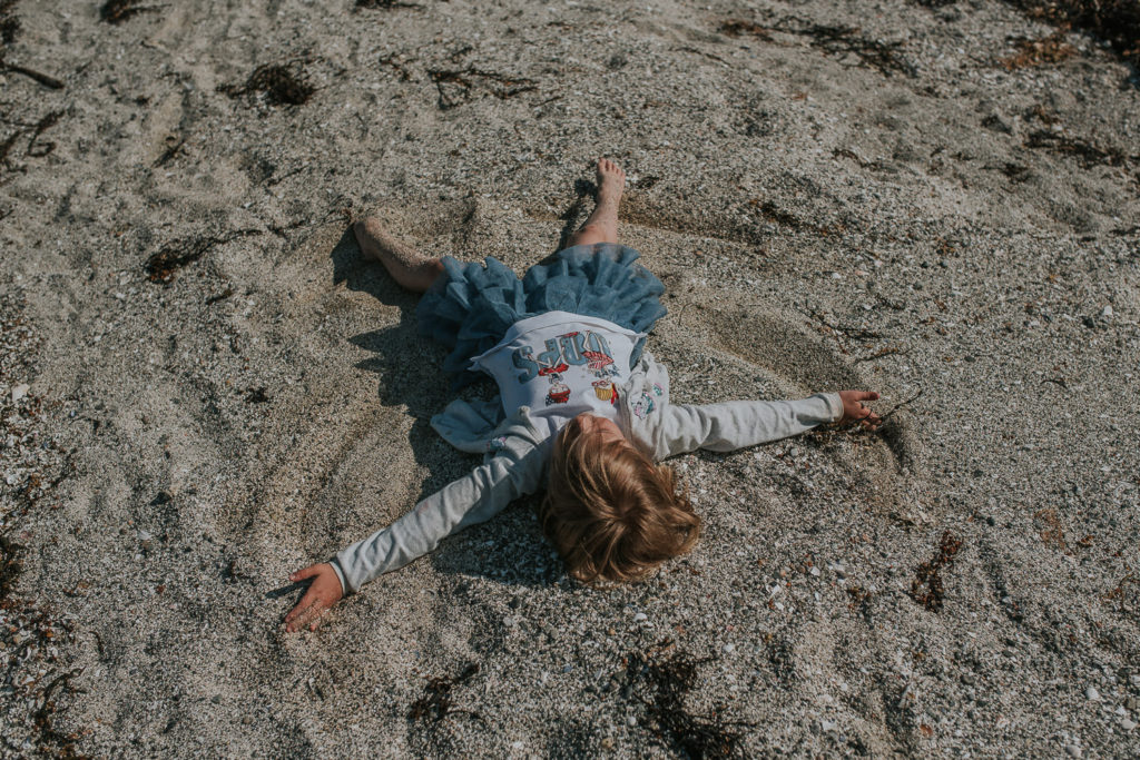 Liten jente lager engler i sand på en strand i Finnmark 
