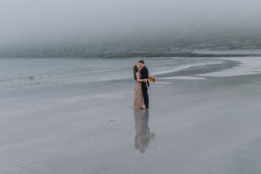 Bride and groom kissing on a secluded beach in Sørøya in Norway on a foggy night