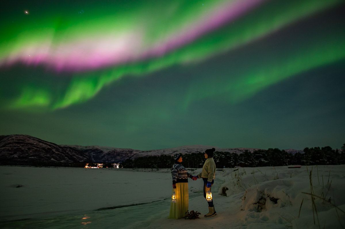 Two brides under a beautiful pink and green aurora borealis on the day of their northern lights elopement in Alta Norway
