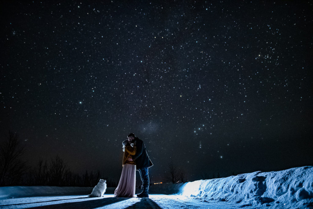 Bride and groom kissing under the stars and their puppy watching them