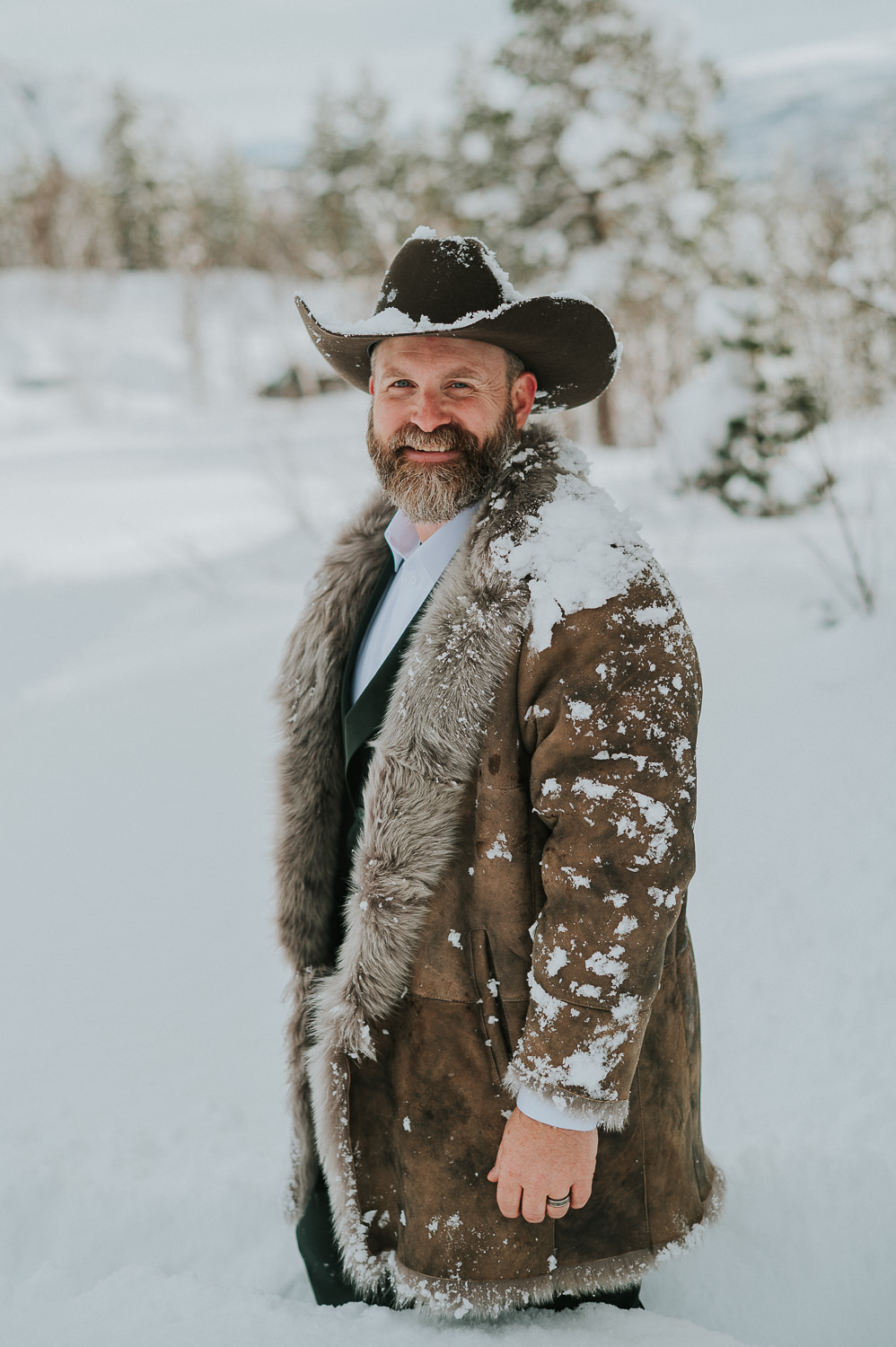 Handsome groom in a cowboy hat and fur coat on the day of his winter elopement in Alta Norway