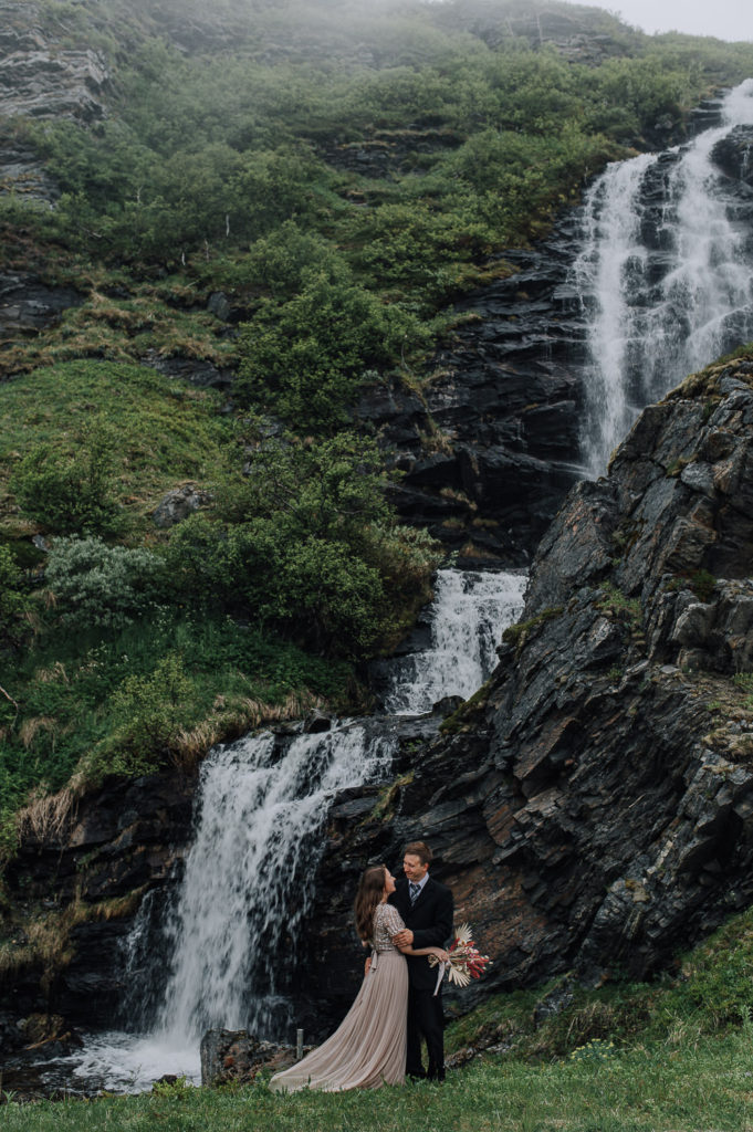 Bride and groom having fun in front of a waterfall on the day of their adventure elopement in Norway