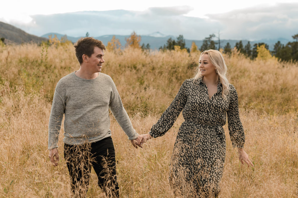 Cute couple holding hands and walking in golden fields in the sunset on the day of their engagement photo session in Norway