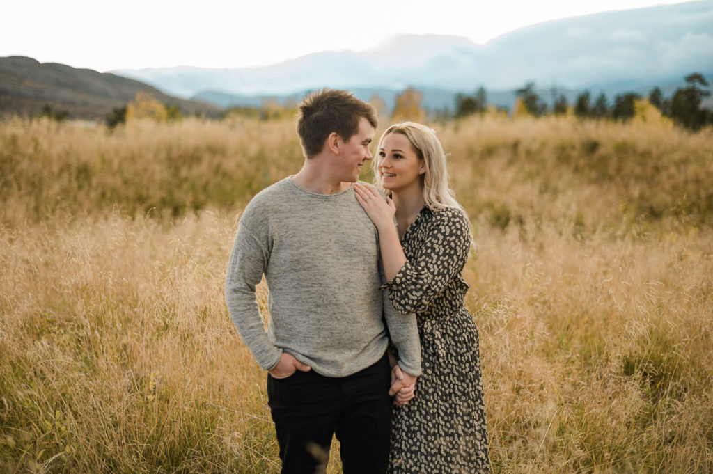 Cute couple hugging each other in beautiful fields on the day of their sunset engagement photo session in Norway