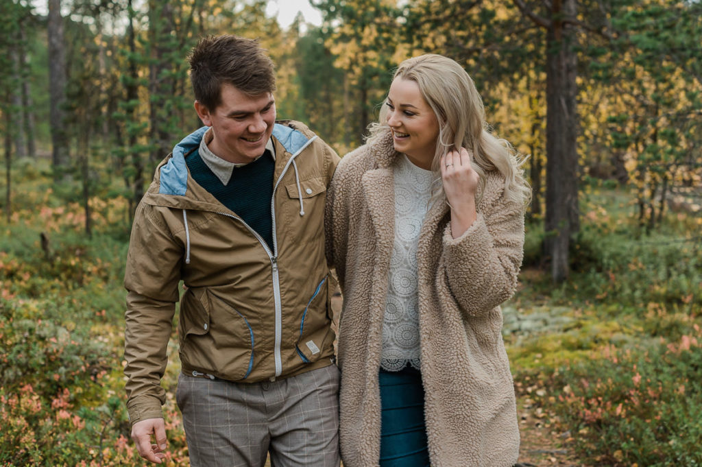 A beautiful couple walking in a colorful forest on the day of their fall engagement photo session 