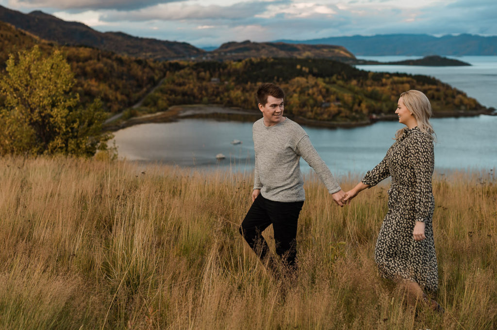 Beautiful couple walking in front of a stunning seaview right after the sunset in Norway - fall engagement photo session