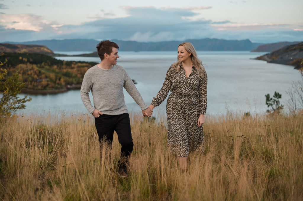 Pretty couple walking in the fields of dried grass on the day of their sunset fall engagement session in Alta Norway