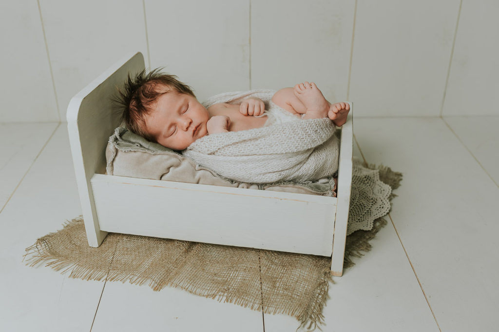Søt nyfødt jente sover i en dukkeseng på fotoshoot i studio hos nyfødtfotograf i Alta