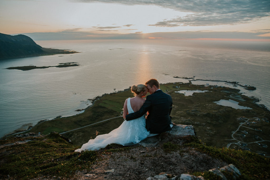 Bride and groom sitting on a mountaintop enjoying the sunset in Lofoten