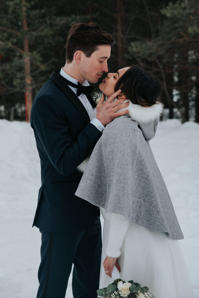 Bride and groom kissing in a winter forest on the day of their elopement 