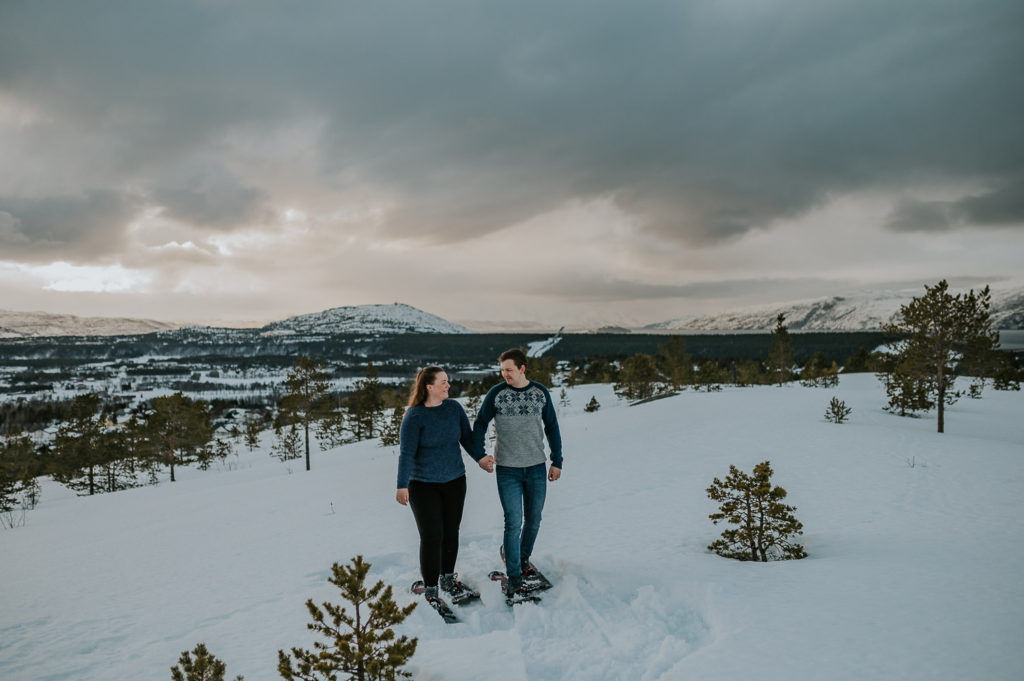Snowshoeing engagement photo session in Alta, Norway - beautiful couple portrait on a mountaintop with snowshoes enjoying nice winter views