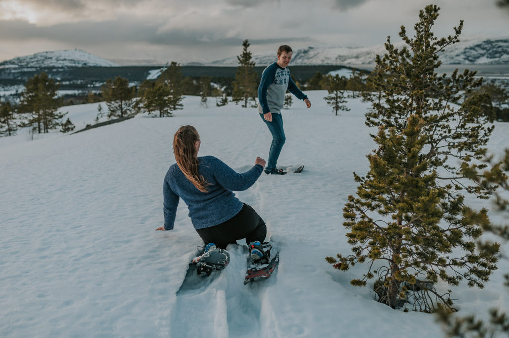 Snowshoeing engagement photo session in Alta, Norway - the bride to be fell down in the snow and the groom to be is helping her up