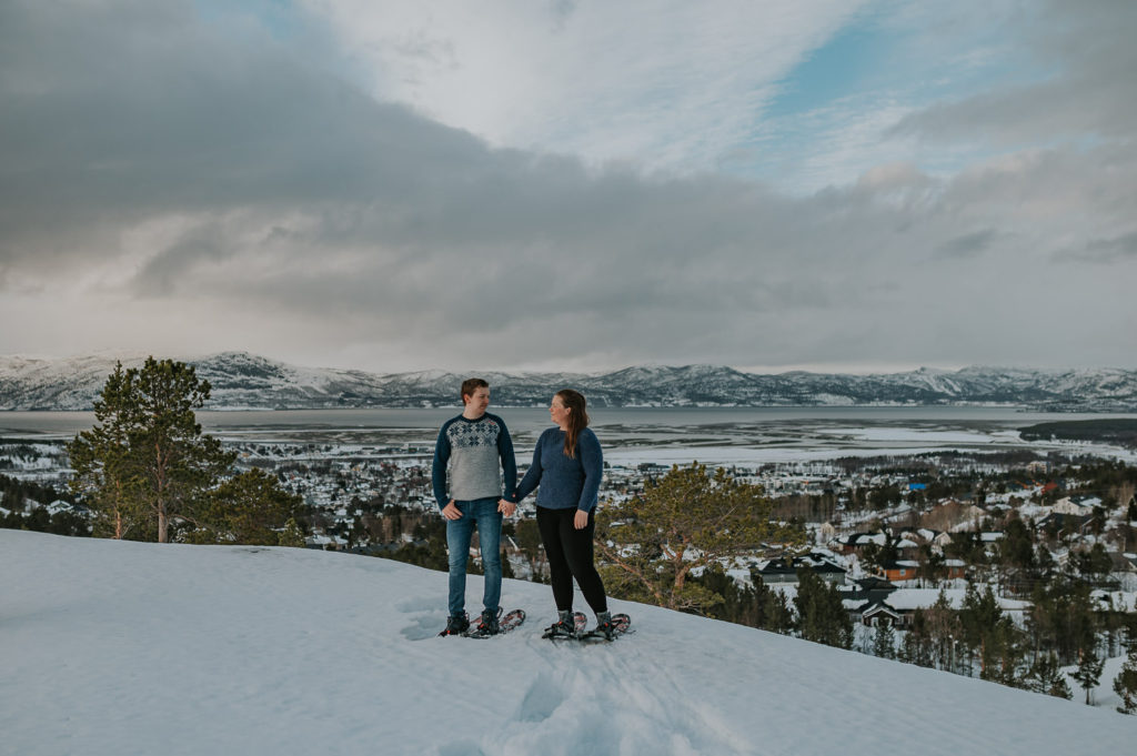 Snowshoeing engagement photo session in Alta, Norway - beautiful couple portrait on a mountaintop overlooking the whole town 