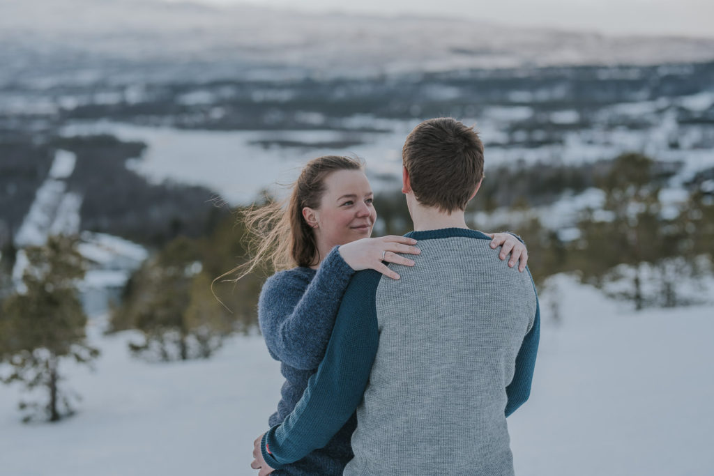 Snowshoeing engagement photo session in Alta, Norway - beautiful couple portrait on a mountaintop when the bride to be is hugging her groom