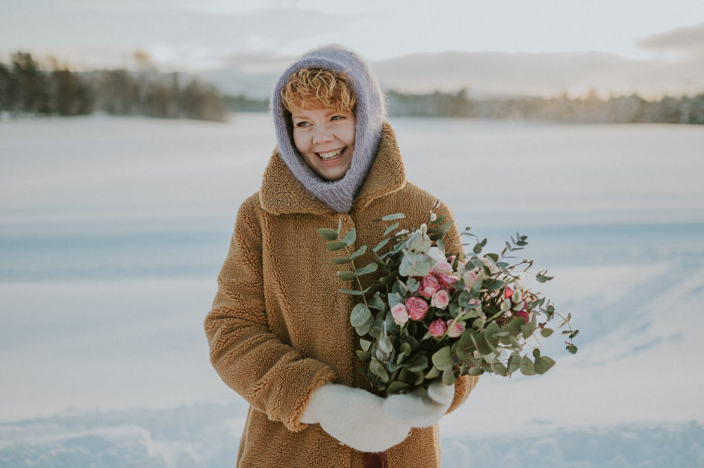 Happy bride is smiling to her groom and holding beautiful winter bouquet on their intimate winter wedding day in Northern Norway