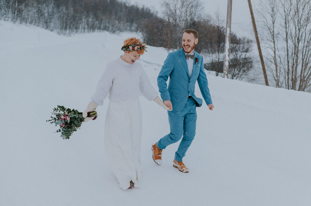 Bridal couple eloping in Norway in winter time running under the snow with a beautiful mountain backdrop