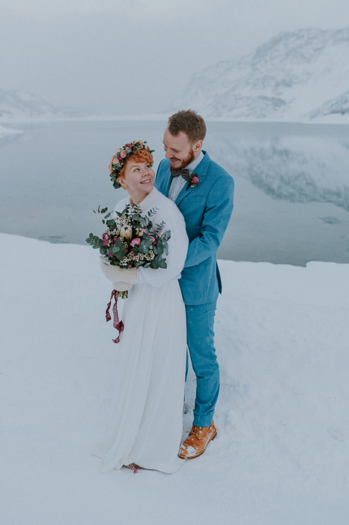 Bride and groom in front of the sea with a view to a fjord and mountains in Alta Norway on the day of their winter elopement