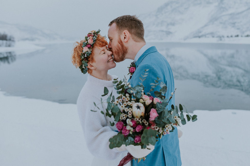 Groom kissing his bride on a cheek - with a beautiful winter landscape in the background