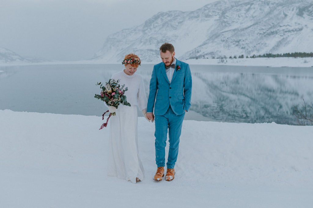 Bridal couple eloping in Norway in winter time walking under the snow with a beautiful mountain backdrop