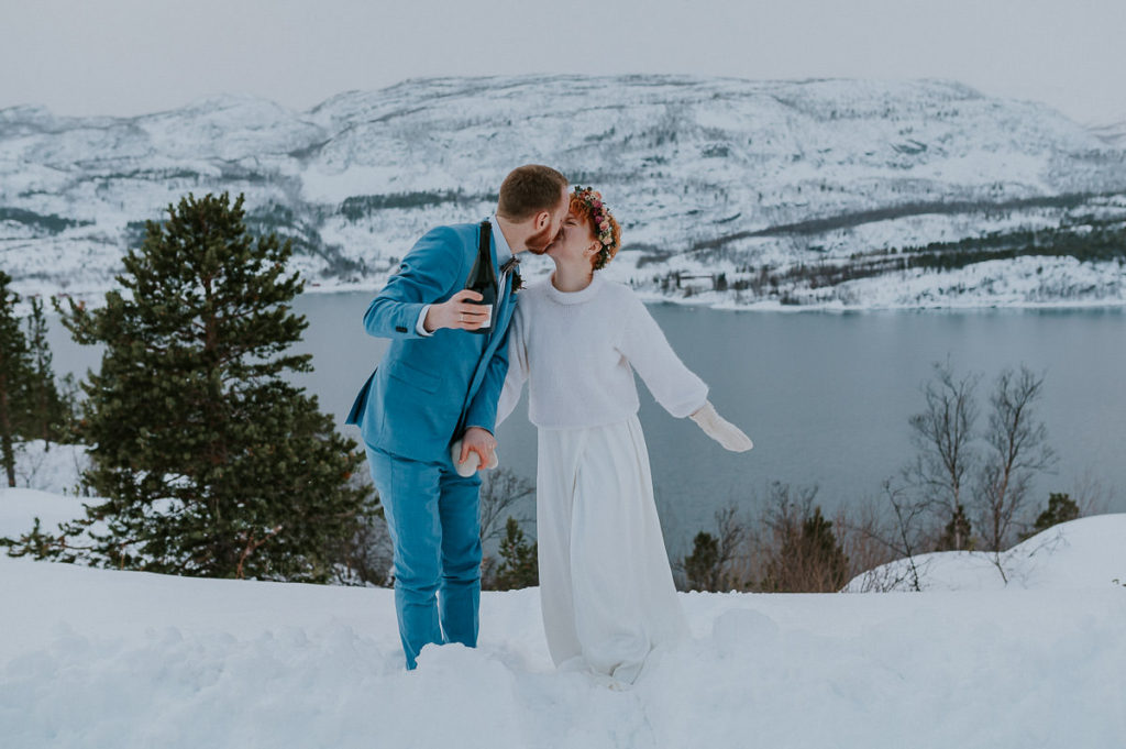 Just married - happy bride and groom on the day of their winter elopement in Norway - kissing in front of beautiful mountain views and fjords