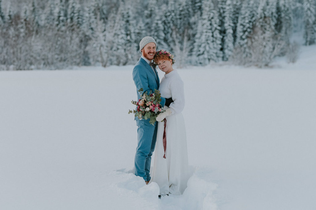 Beautiful portrait of a bride and groom in front of gorgeous winter forest on the day of their intimate elopement wedding in Alta Norway