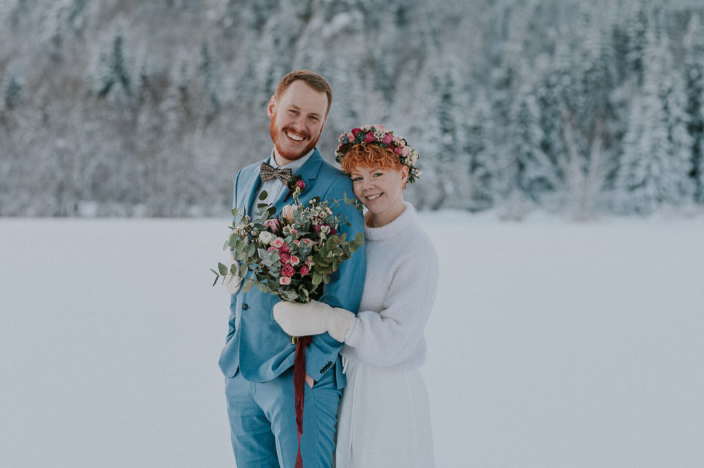 Beautiful portrait of a bride and groom in front of gorgeous winter forest on the day of their intimate elopement wedding in Alta Norway