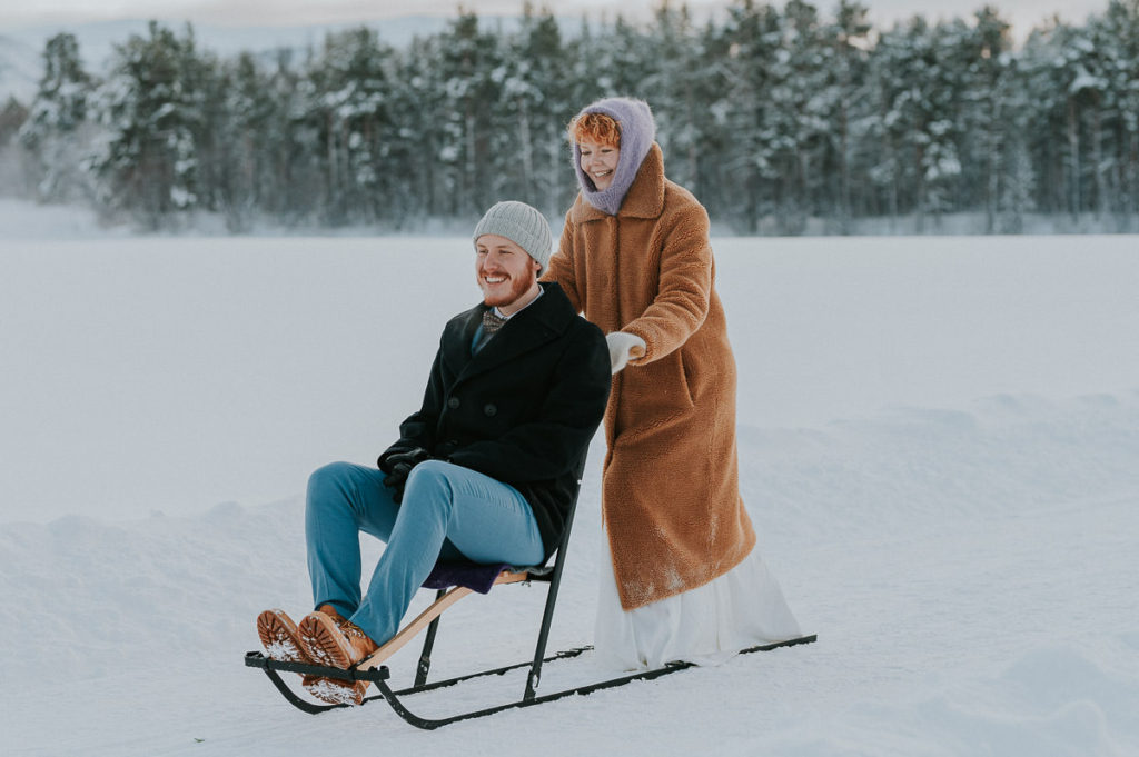 Bride pushes a kicksled with her groom on her winter wedding day in Northern Norway