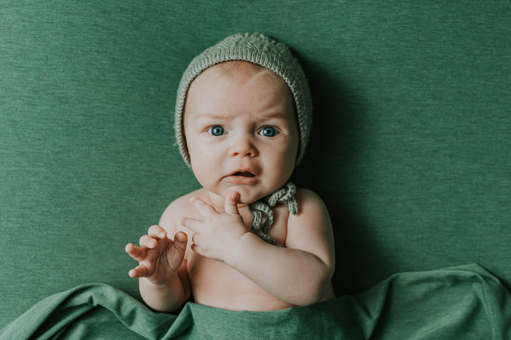 Skjønn 3 måneder gammel jente på grønn fotobakgrunn og med grønn lue på